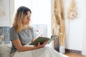 a-lady-reading-a-book-while-siting-on-her-bed