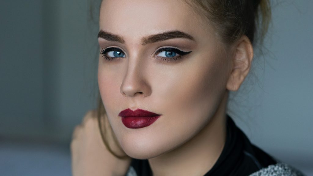 A close-up captures a woman's striking blue eyes, bold eyeliner, and deep red lips