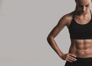 Portrait-of-sporty-young-woman-with-muscular-body-posing-against-a-gray-background