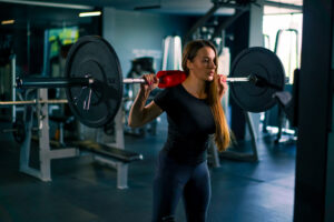 portrait of a concentrated fitness woman doing a heavy shoulder press exercise with a barbell in gym training muscle groups