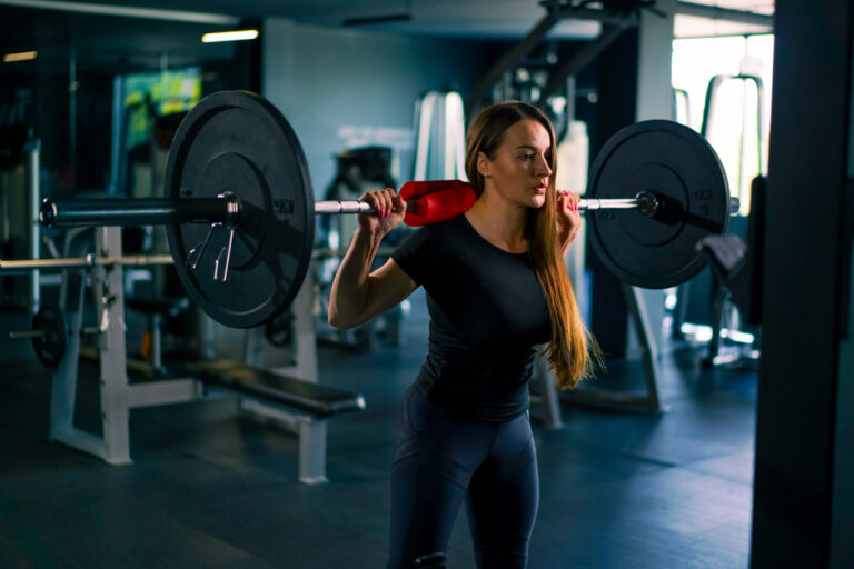 portrait of a concentrated fitness woman doing a heavy shoulder press exercise with a barbell in gym training muscle groups