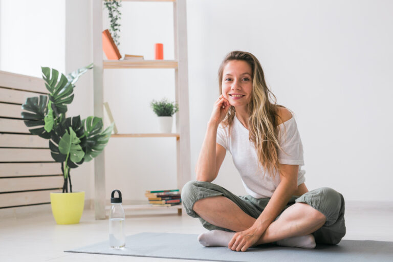 Positive girl sitting on fitness mat resting after pilates or yoga practice.