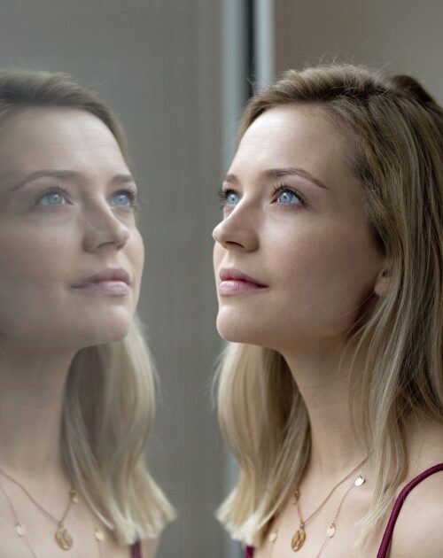 Portrait of blond young woman and her reflection on windowpane