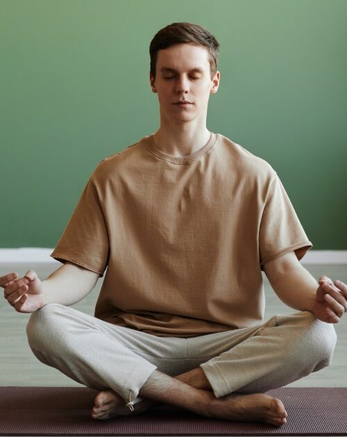 Young man meditating indoors sitting in lotus position with eyes closed