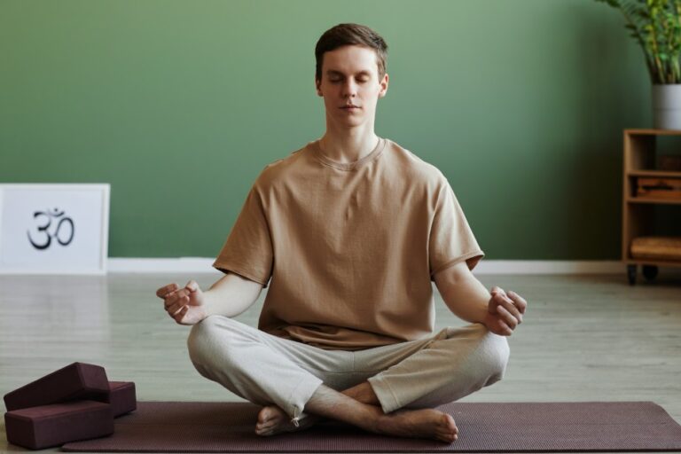 Young man meditating indoors sitting in lotus position with eyes closed