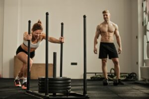 Athletic-woman-making-effort-while-pushing-gym-sled-with-weights-on-cross-training