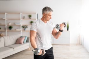 Strong-mature-man-doing-dumbbell-workout-at-home-working-on-arms-strength-and-looking-at-his-biceps