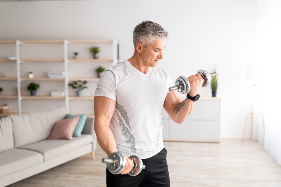 Strong-mature-man-doing-dumbbell-workout-at-home-working-on-arms-strength-and-looking-at-his-biceps