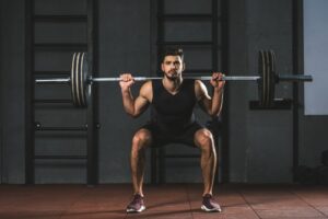 Young-bodybuilder-doing-exercise-with-barbell-on-shoulders-in-gym
