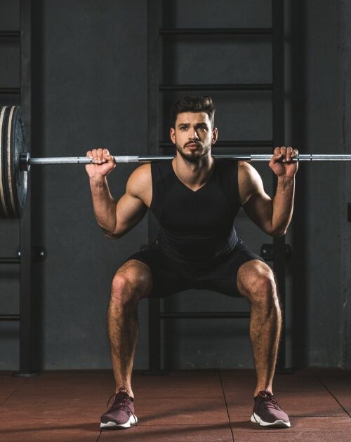 Young-bodybuilder-doing-exercise-with-barbell-on-shoulders-in-gym