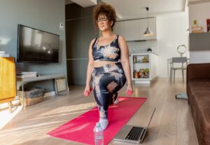 Young-plus-size-woman-at-home-doing-exercise-in-front-of-open-laptop