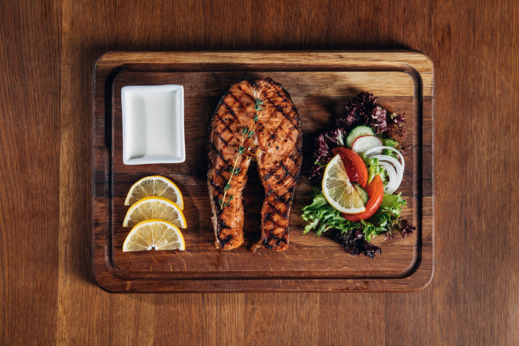 top view of grilled salmon steak served on wooden board with lemon and salad