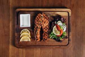 top view of grilled salmon steak served on wooden board with lemon and salad