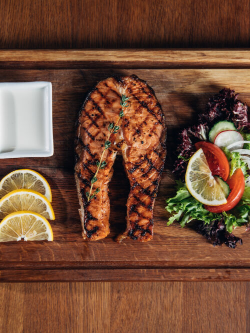 top view of grilled salmon steak served on wooden board with lemon and salad