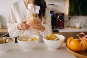 Close-up of the hands of a girl who makes a detox cocktail of fruit in the kitchen
