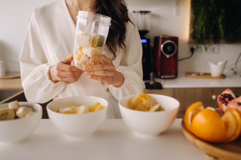 Close-up of the hands of a girl who makes a detox cocktail of fruit in the kitchen