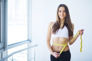 Smiling Woman Measures Her Waist in Bright Studio